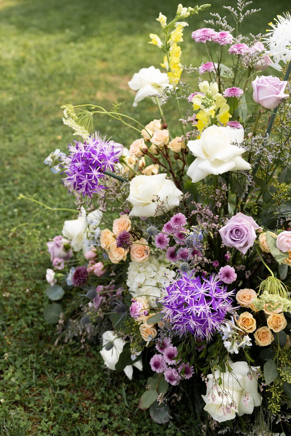 Elegant floral arrangements featuring white, purple, and peach roses with mixed greenery displayed on grass.