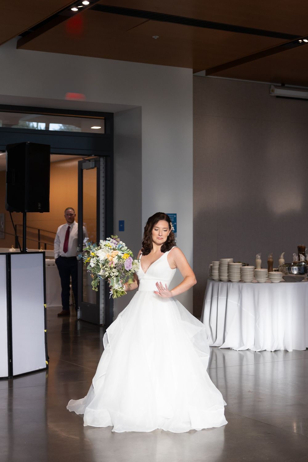 A bride in a flowing white ballgown poses in an elegant reception venue with white tables and modern decor.