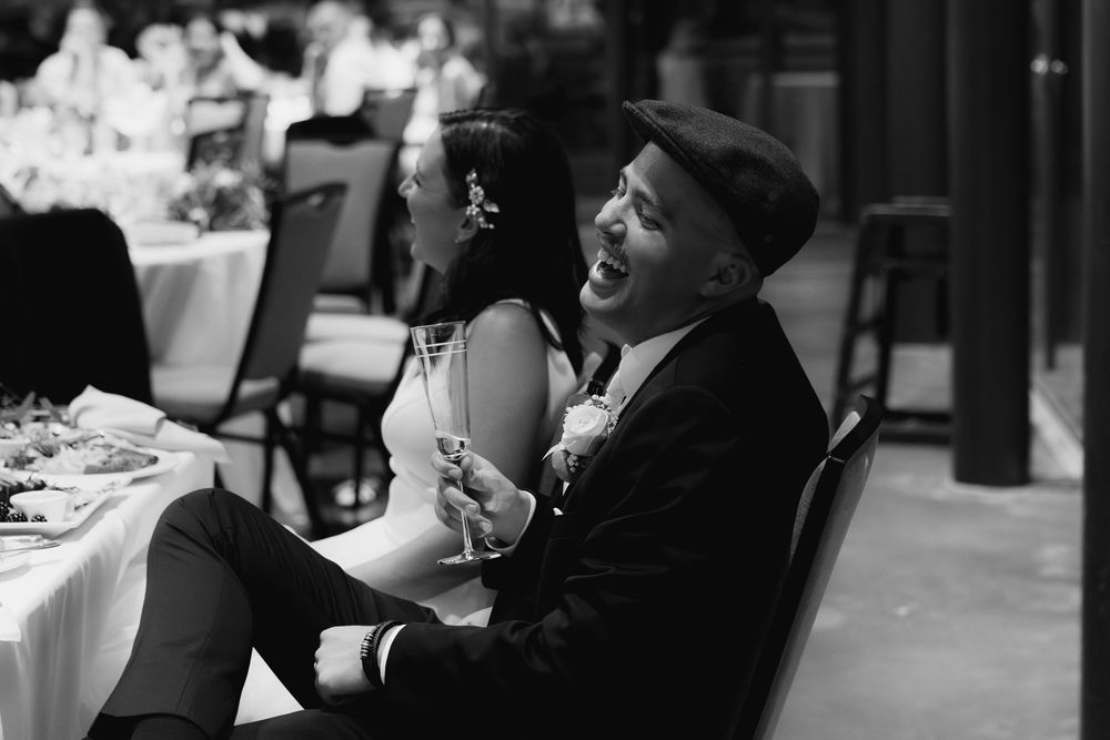 A guest in a black suit and cap enjoys a moment during a wedding reception.