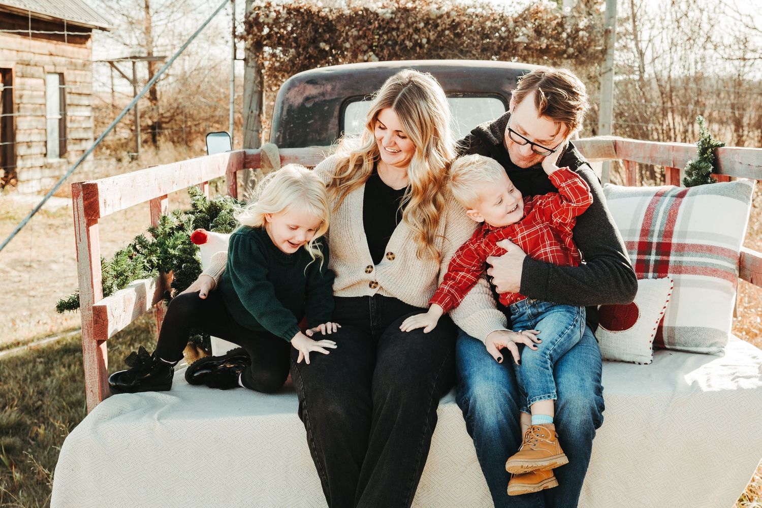 Happy family of four sitting on vintage truck tailgate during festive Christmas photo session.