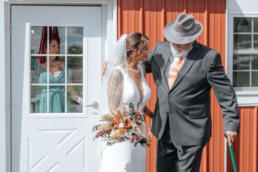 A tender moment between a bride and someone in formal attire in front of a red barn door.