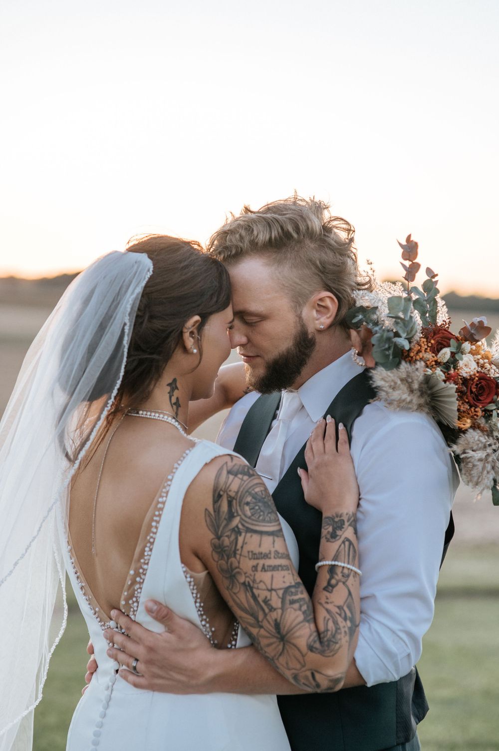An intimate wedding portrait showing a couple in close embrace with visible tattoos and formal attire.