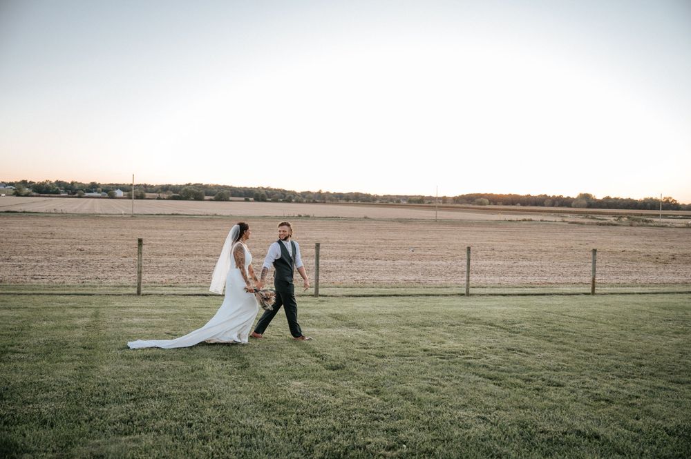 A wedding ceremony setup in a rustic outdoor venue with white chairs and a gazebo overlooking open fields.