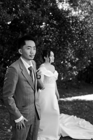 A black and white wedding photo series showing a couple outdoors with lush greenery in the background.