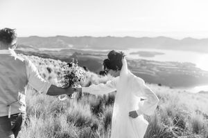 Black and white photo of couple walking through scenic mountain meadow with wildflowers and rolling hills, Christchurch wedding helicopter