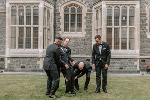 A wedding party poses in front of a grand Gothic-style stone building with ornate windows and architecture.
