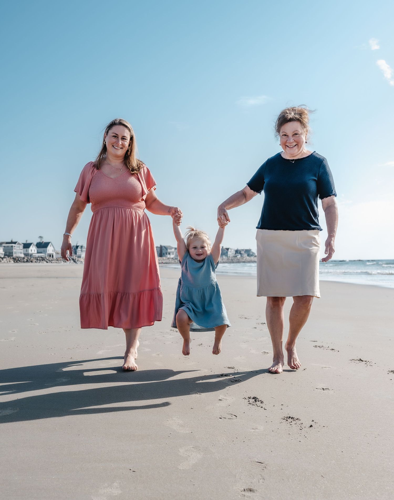 Family photo session at Wells Beach, Maine capturing a child swinging between grandmother and mother during a joyful moment