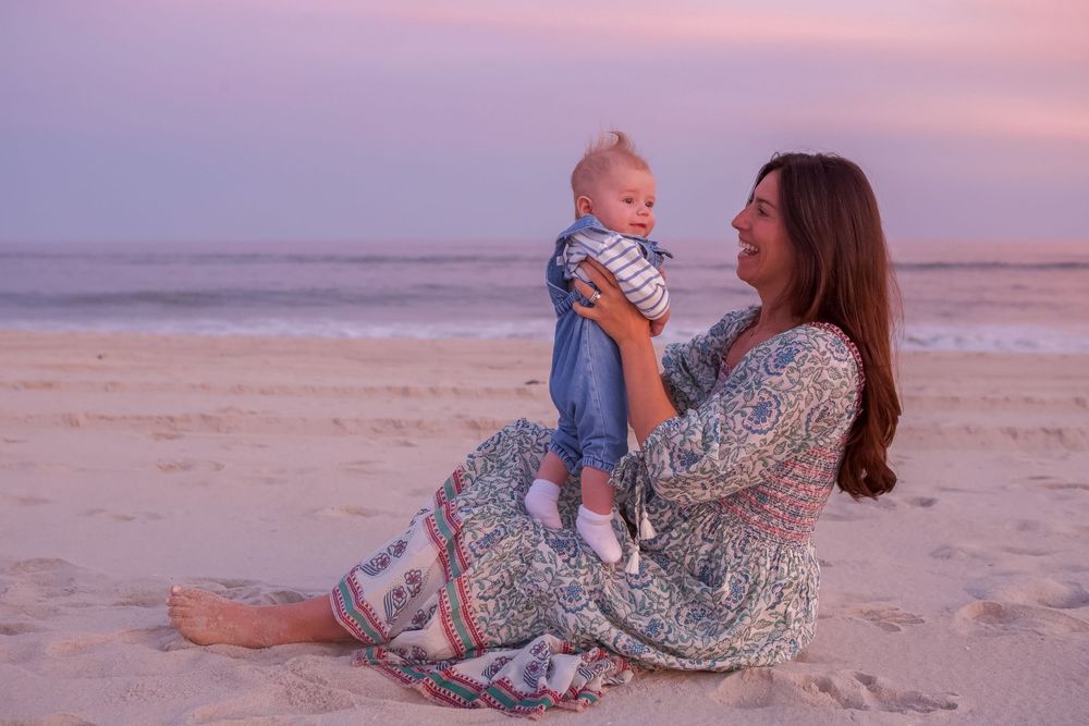 A tender moment shared between parent and child on a beach at sunset with soft pink sky and rolling waves.