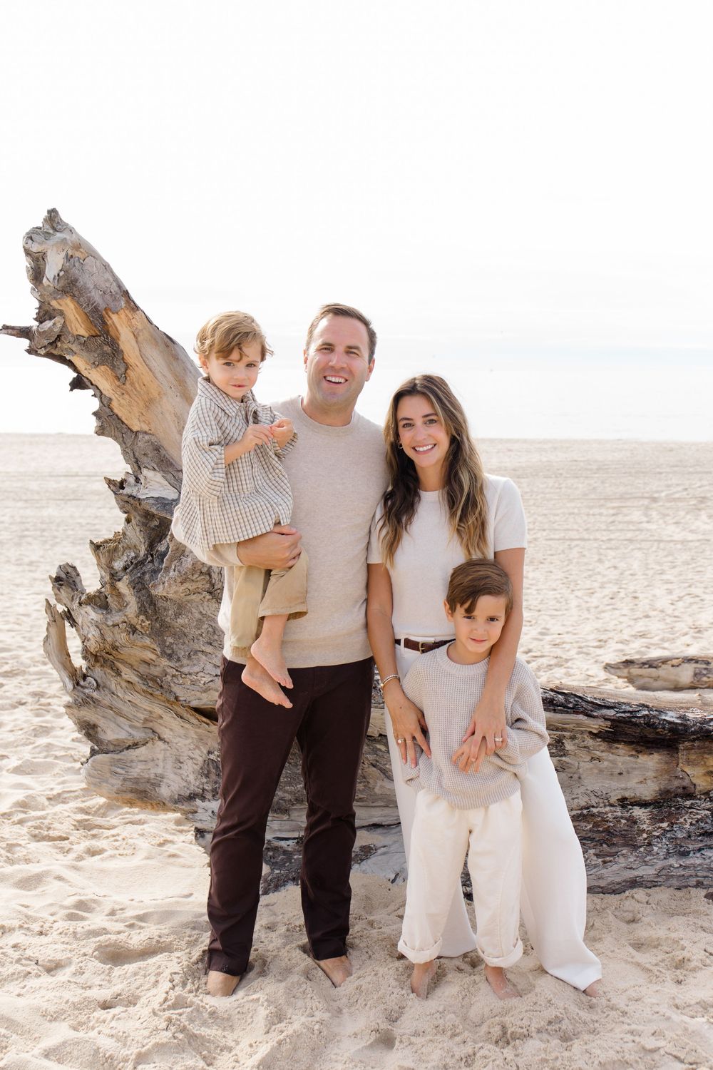A family poses together on a sandy beach next to driftwood during golden hour.