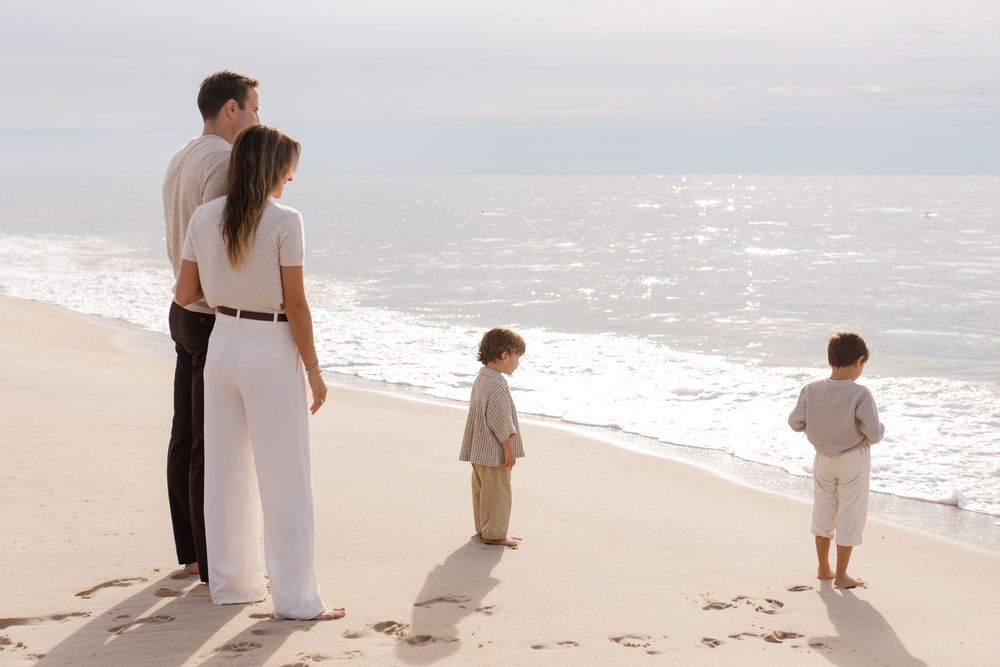Family of four standing together on a peaceful beach shoreline while looking out at the ocean waves.