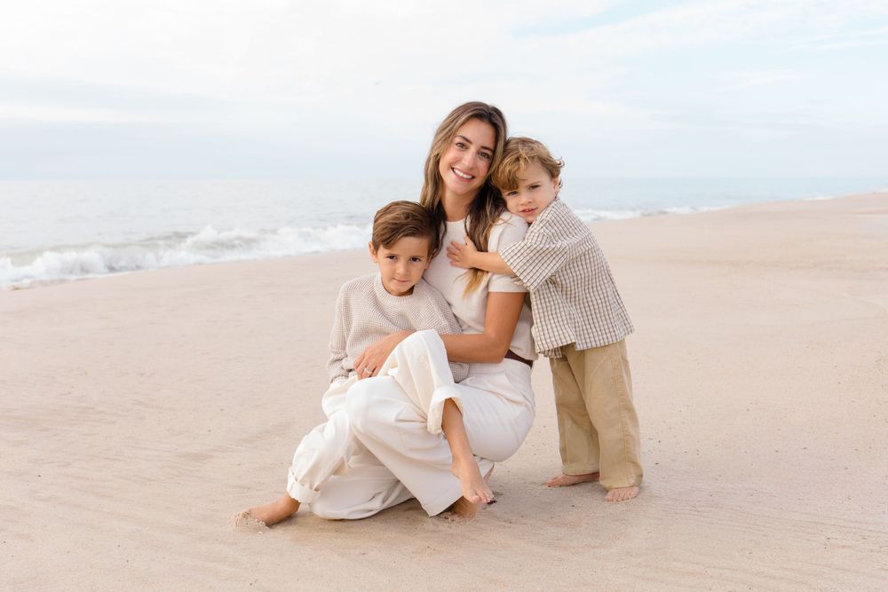 A loving family moment captured on a peaceful beach with soft sand and gentle waves in the background.