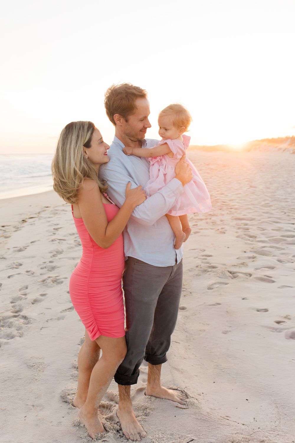 Family enjoying a sunset walk together on a sandy beach in matching coral and grey outfits.