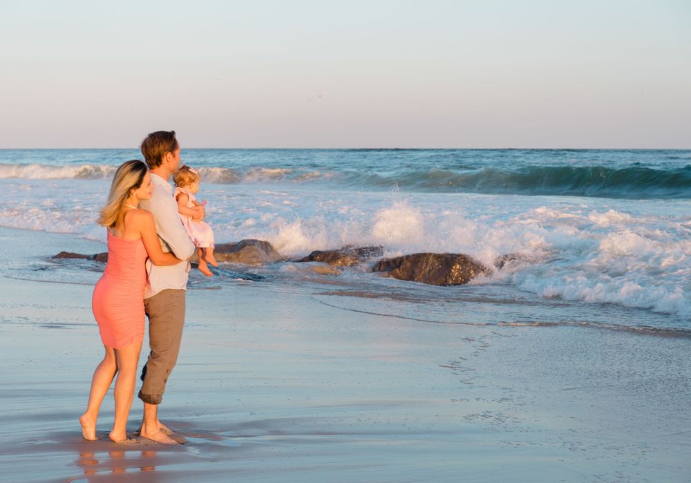 People play and splash in the waves at sunset on a beach with crashing surf and orange-tinted skies.