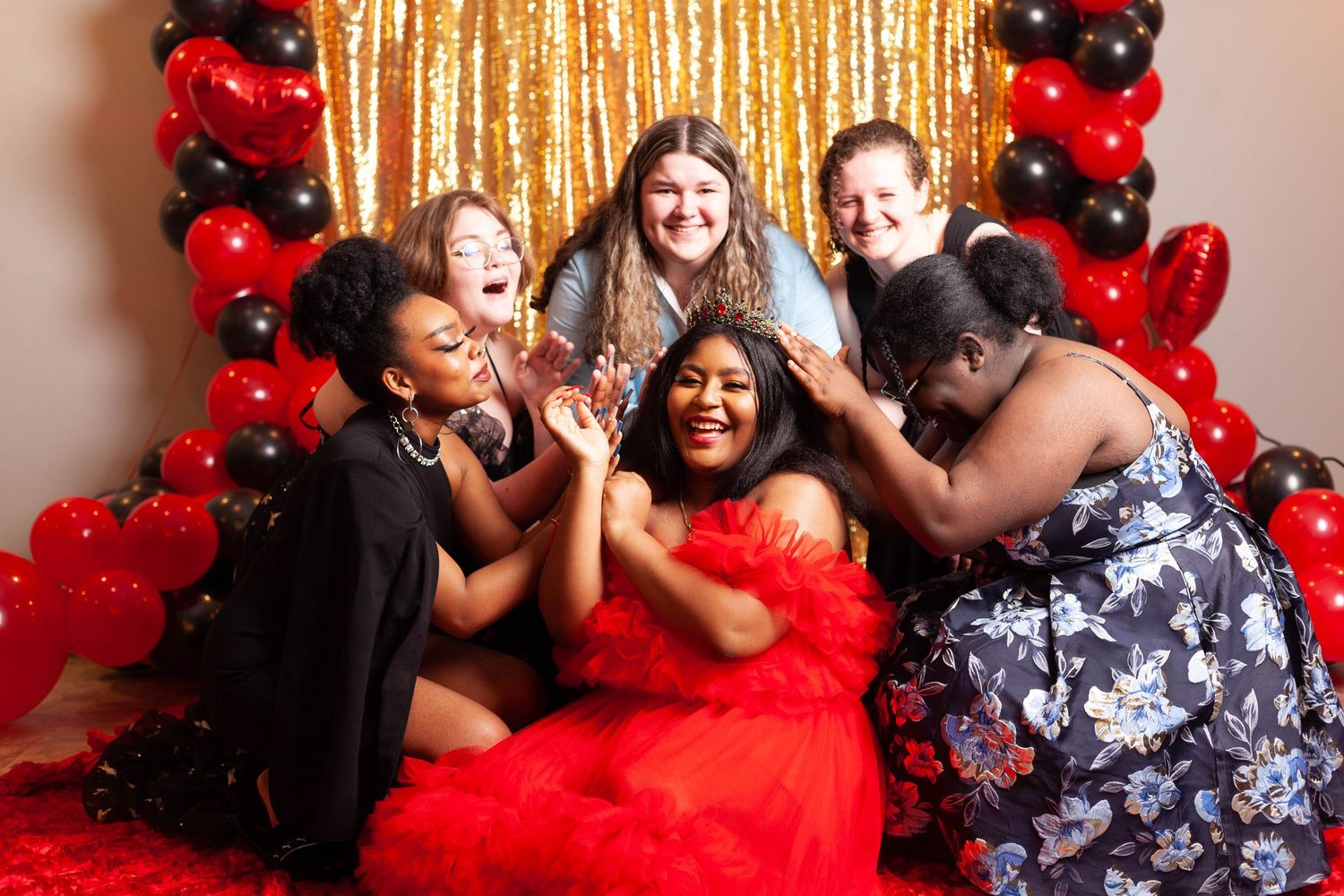 A group wearing red and black outfits poses joyfully against a backdrop of red and black balloons.
