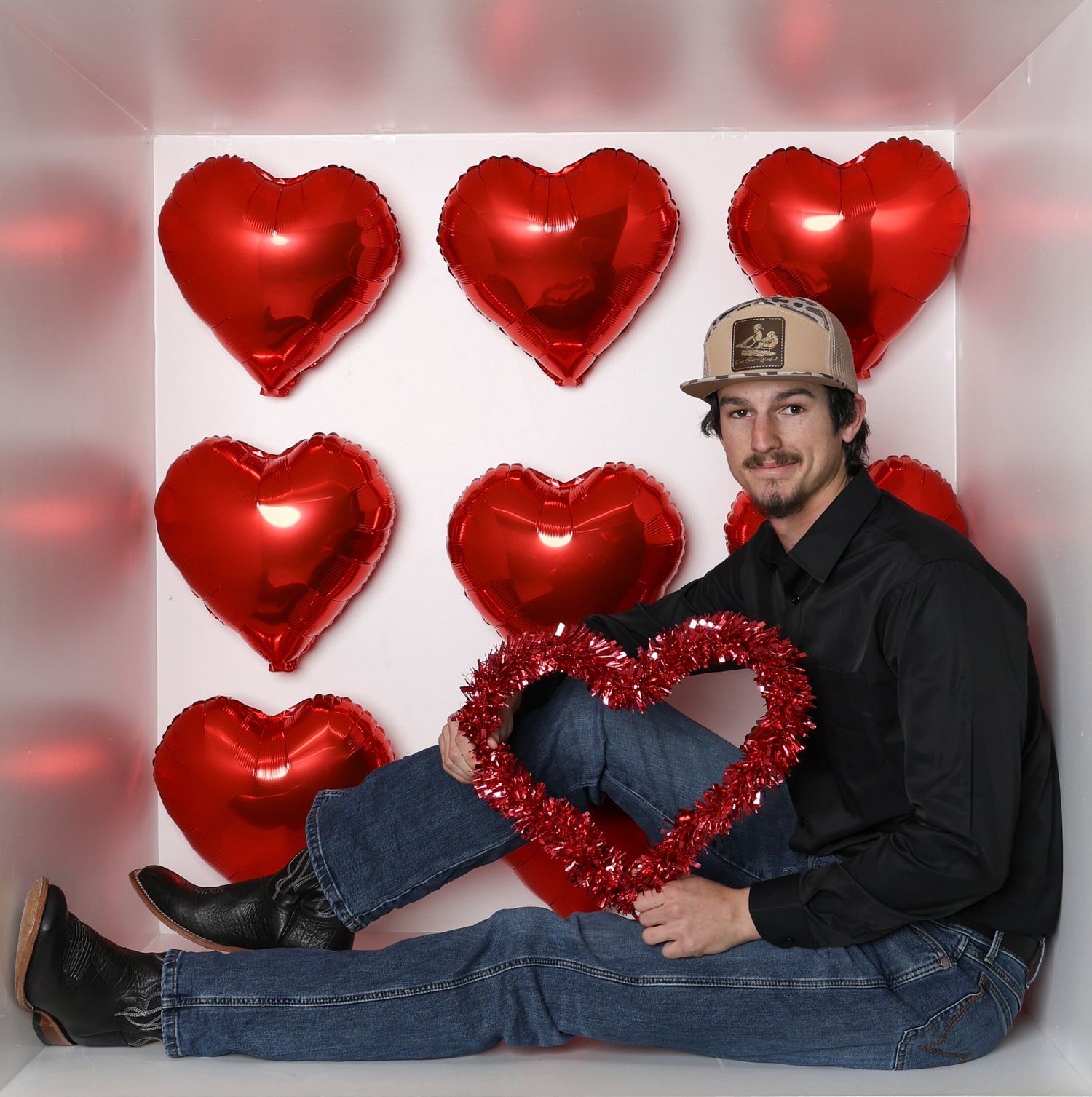 Casual Valentine's photo setup with red heart decorations and two people in relaxed poses. Box photography session