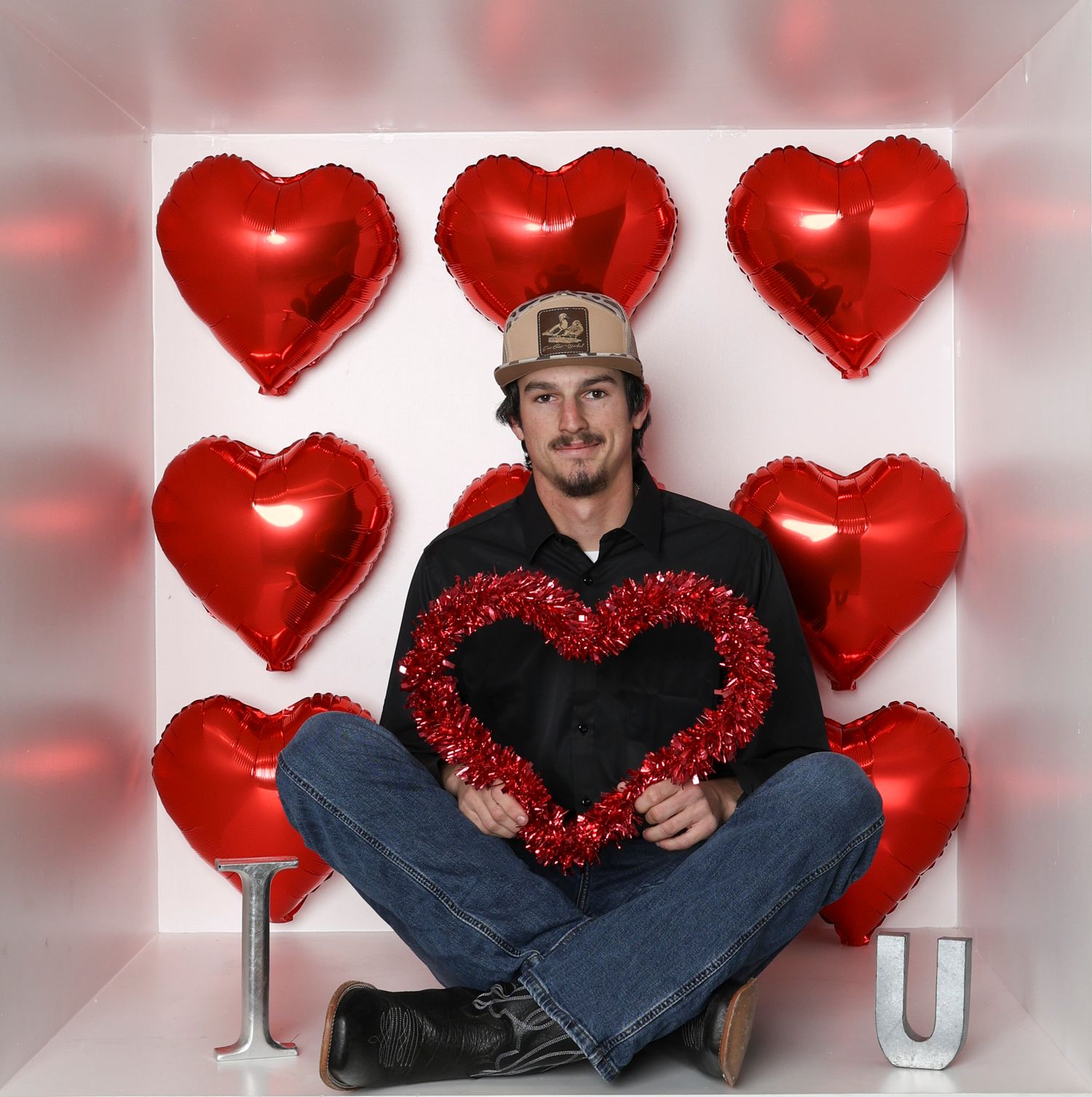 Valentine's setting with red heart balloons and someone sitting cross-legged in casual attire. Box photography session