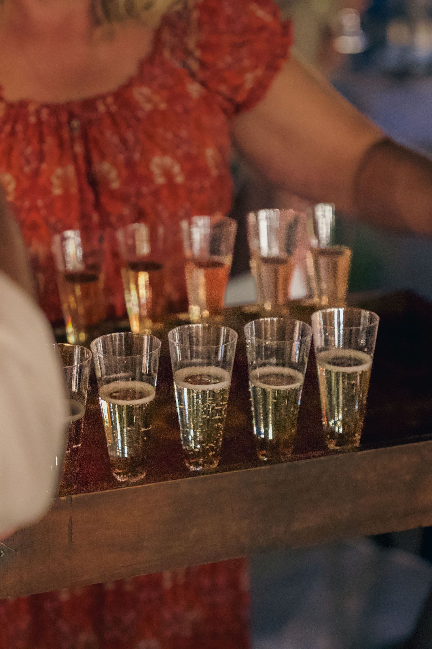 A row of small shot glasses filled with clear liquid arranged on a dark wooden bar surface.