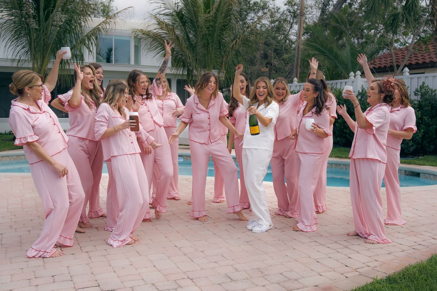 Wedding party members in matching pink dresses dance in a choreographed line by a swimming pool.