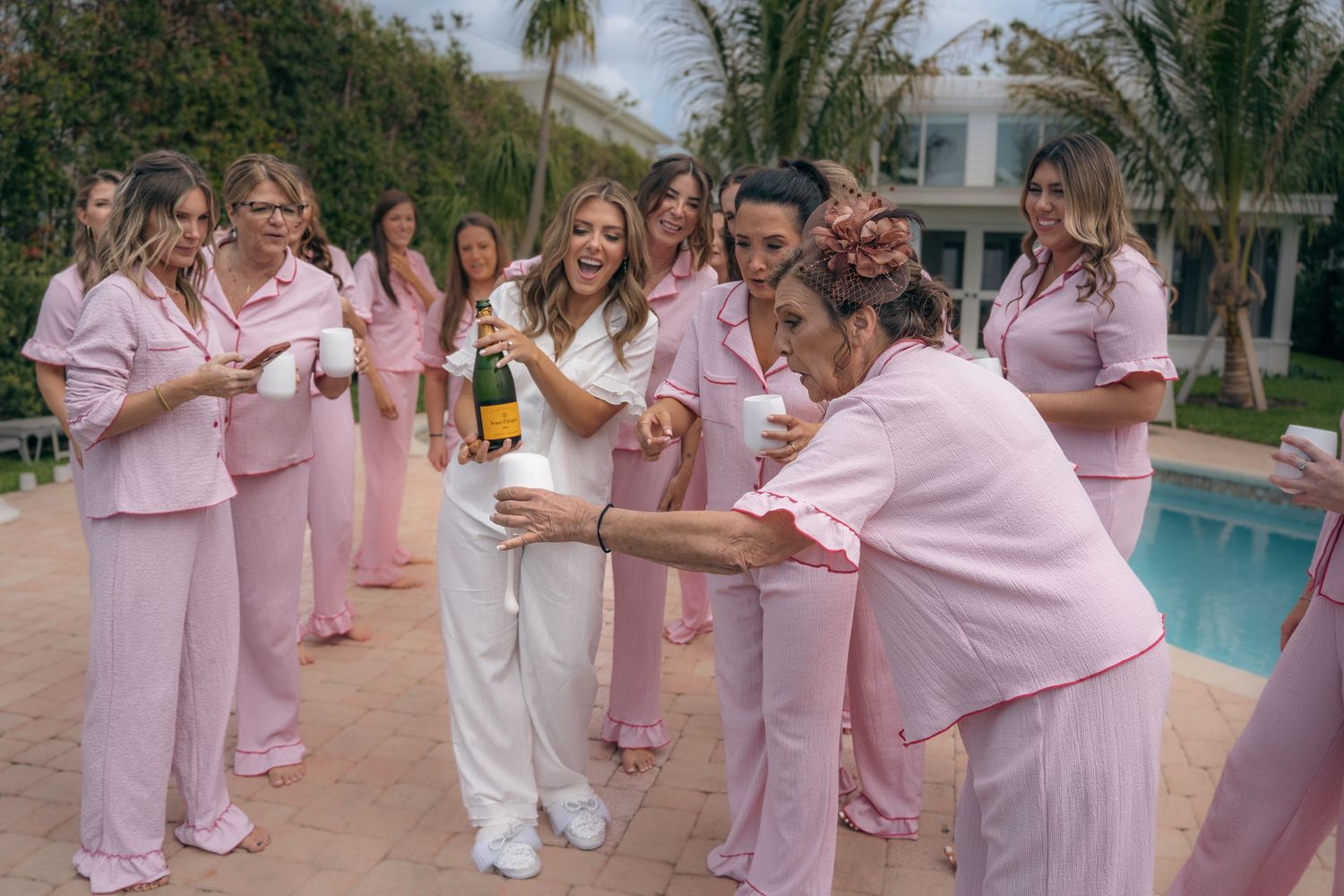 Group of people in matching pink outfits dancing and celebrating by a swimming pool on a sunny day.