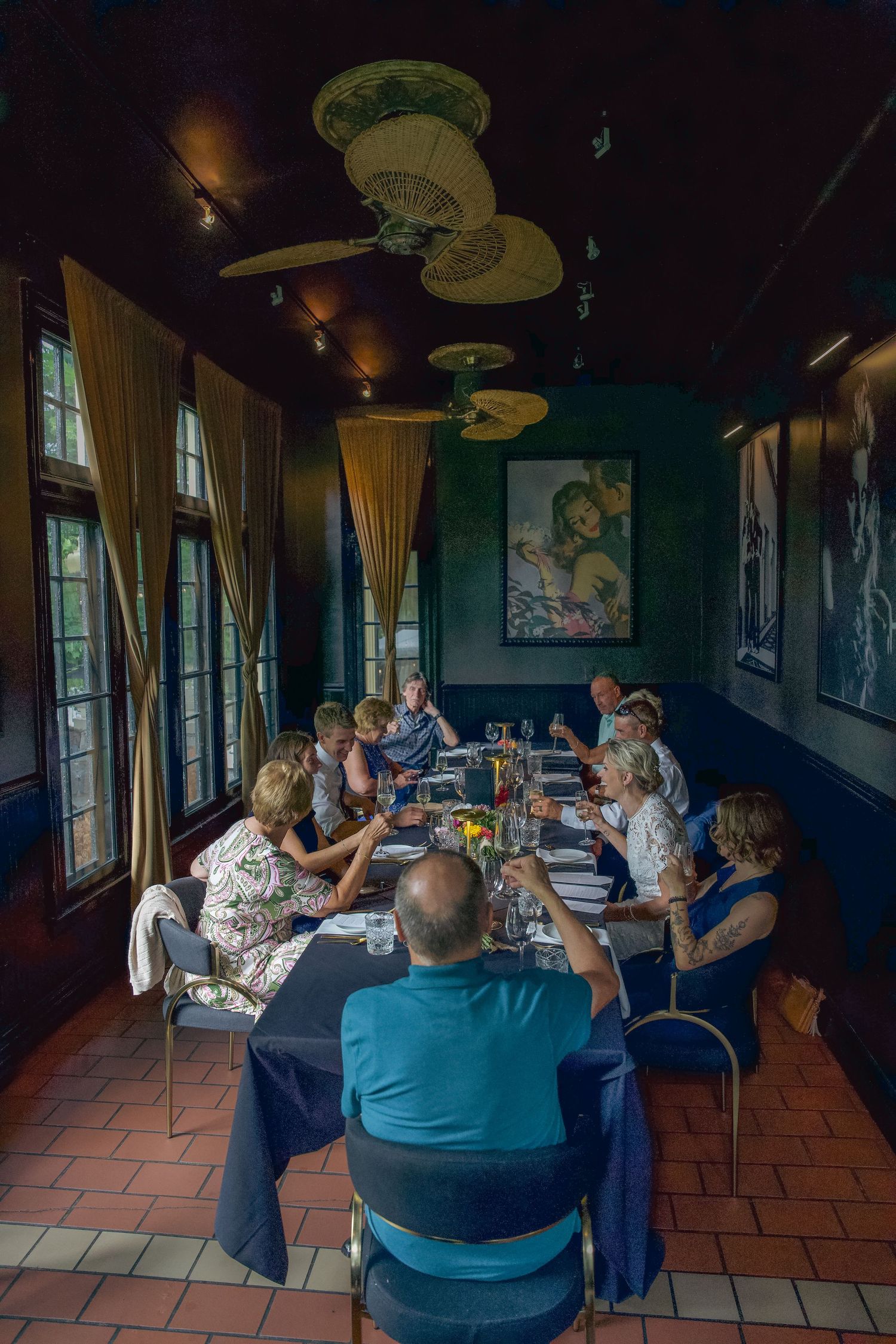 A group of diners seated at a long table in a dimly lit restaurant with decorative ceiling fans and green walls.