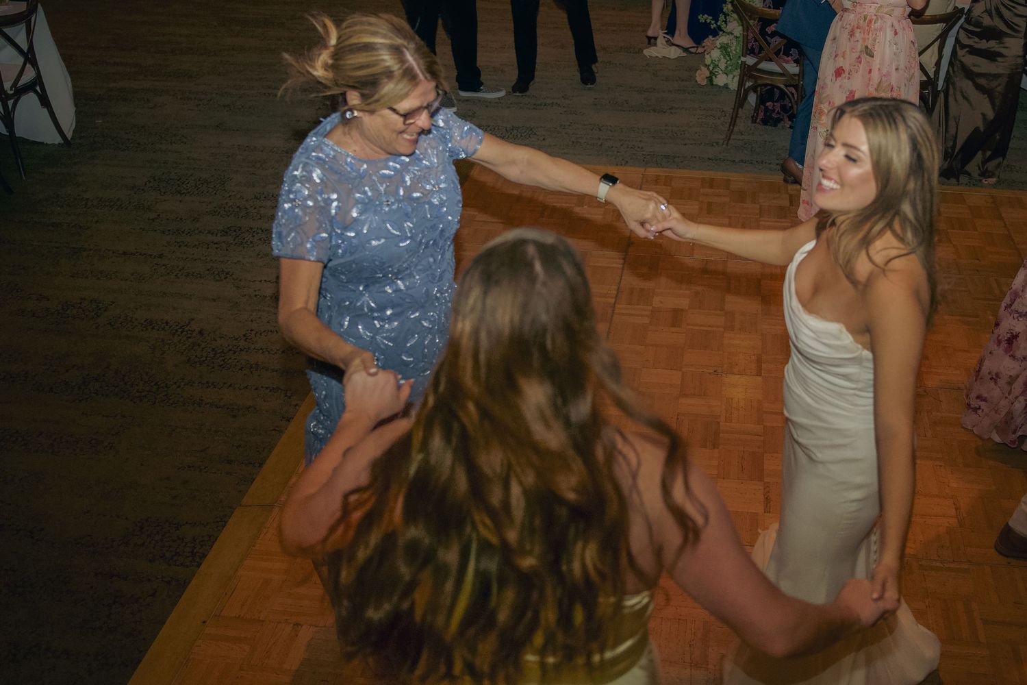People dancing together on a wooden dance floor at a celebration event with one wearing a sparkly blue top.