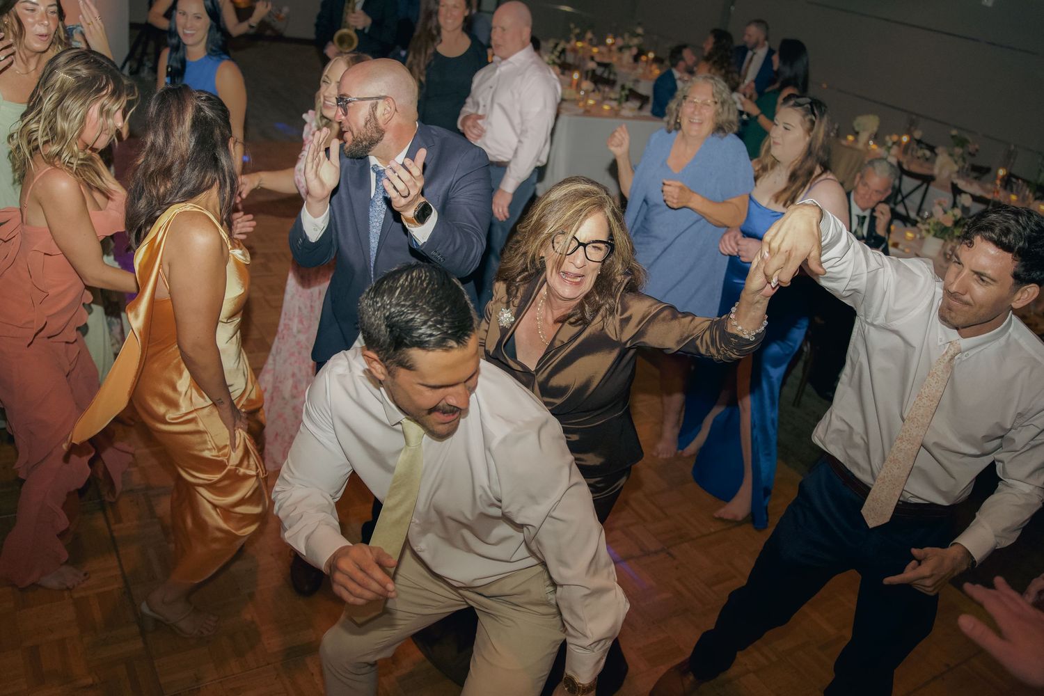 Guests dancing and celebrating at a wedding reception on a dimly lit dance floor.