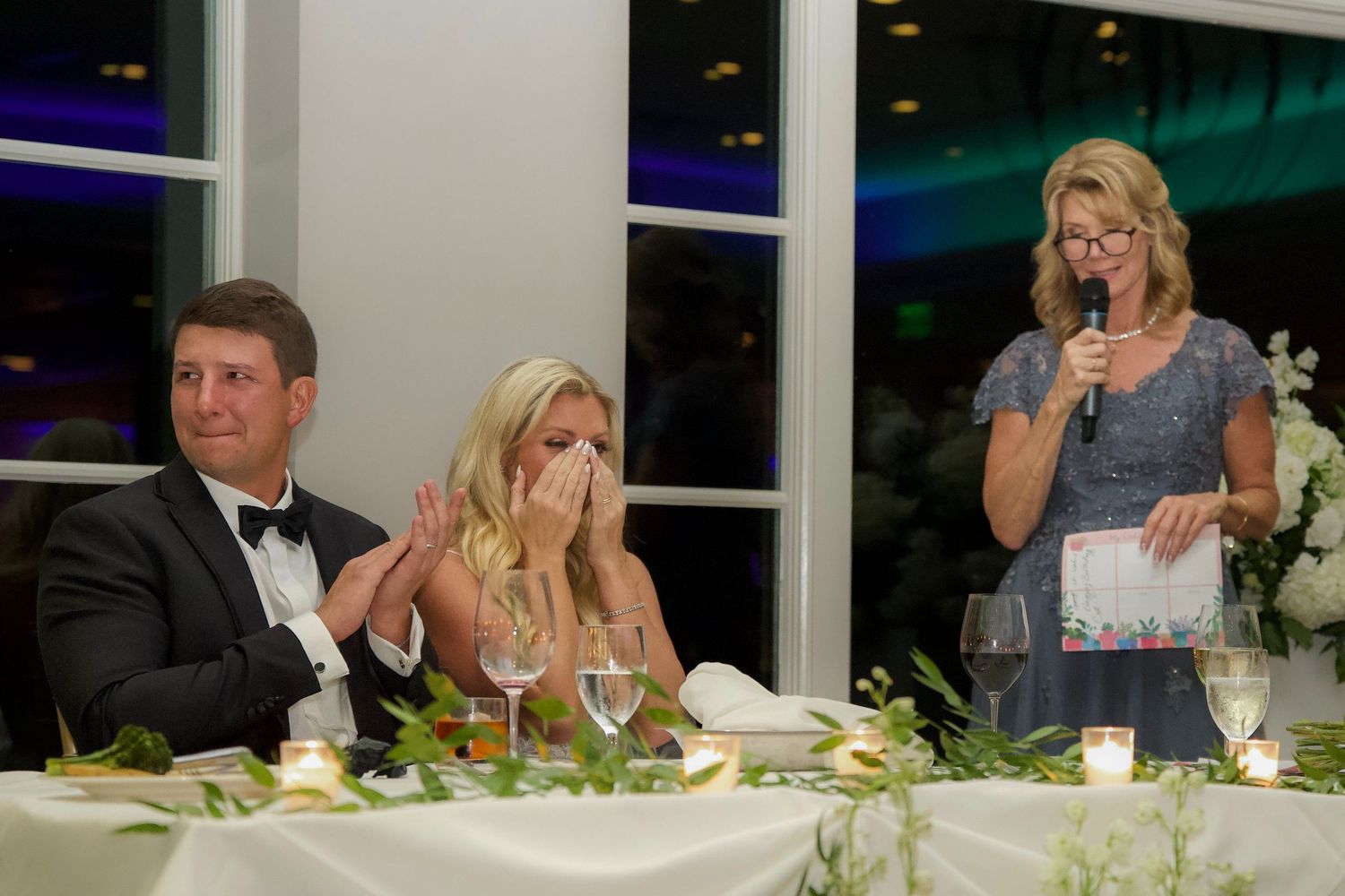 Wedding reception guests seated at a long table during dinner and speeches at an elegant evening event.