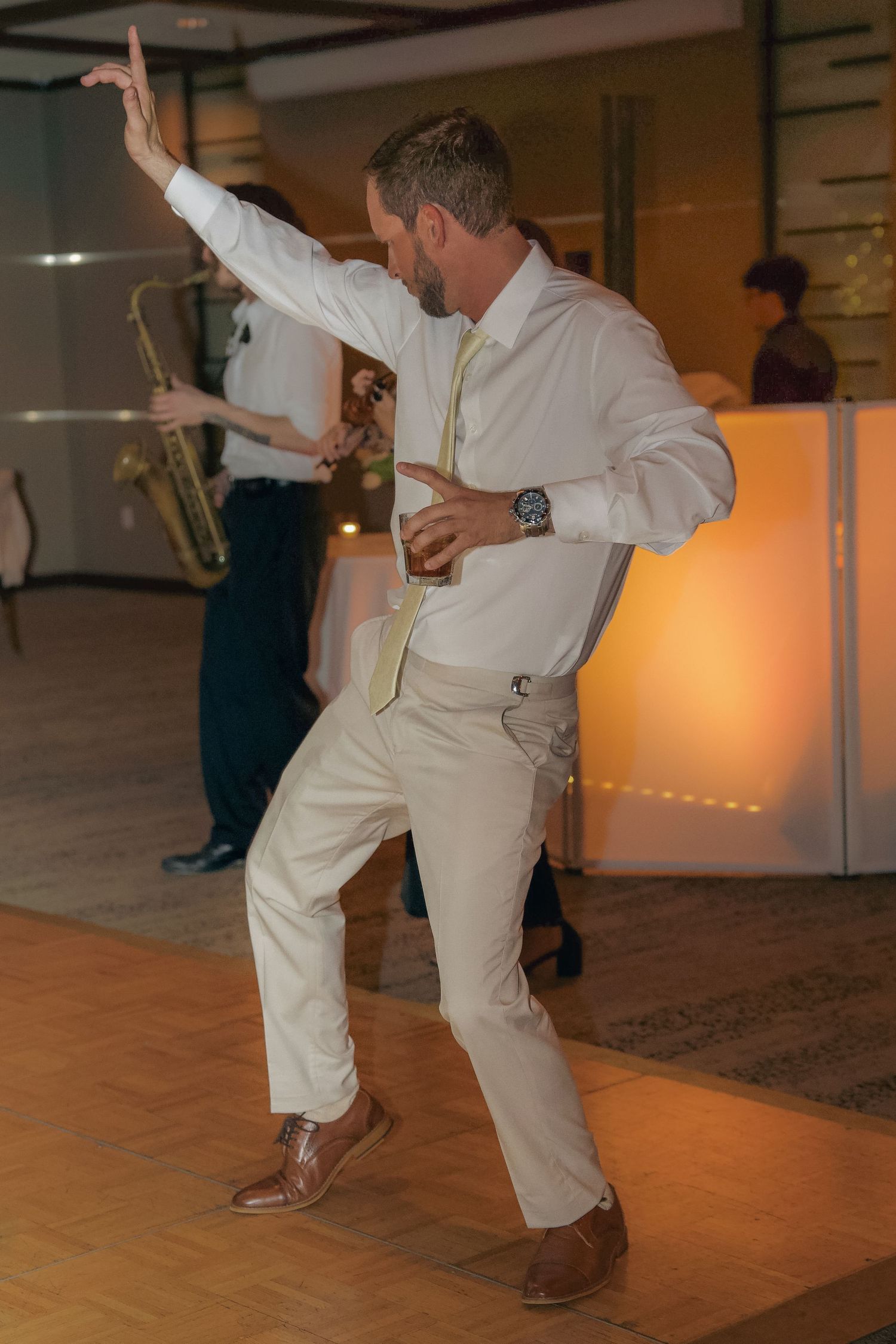 A person in white clothing performs a dynamic dance move on a wooden floor in an indoor space.