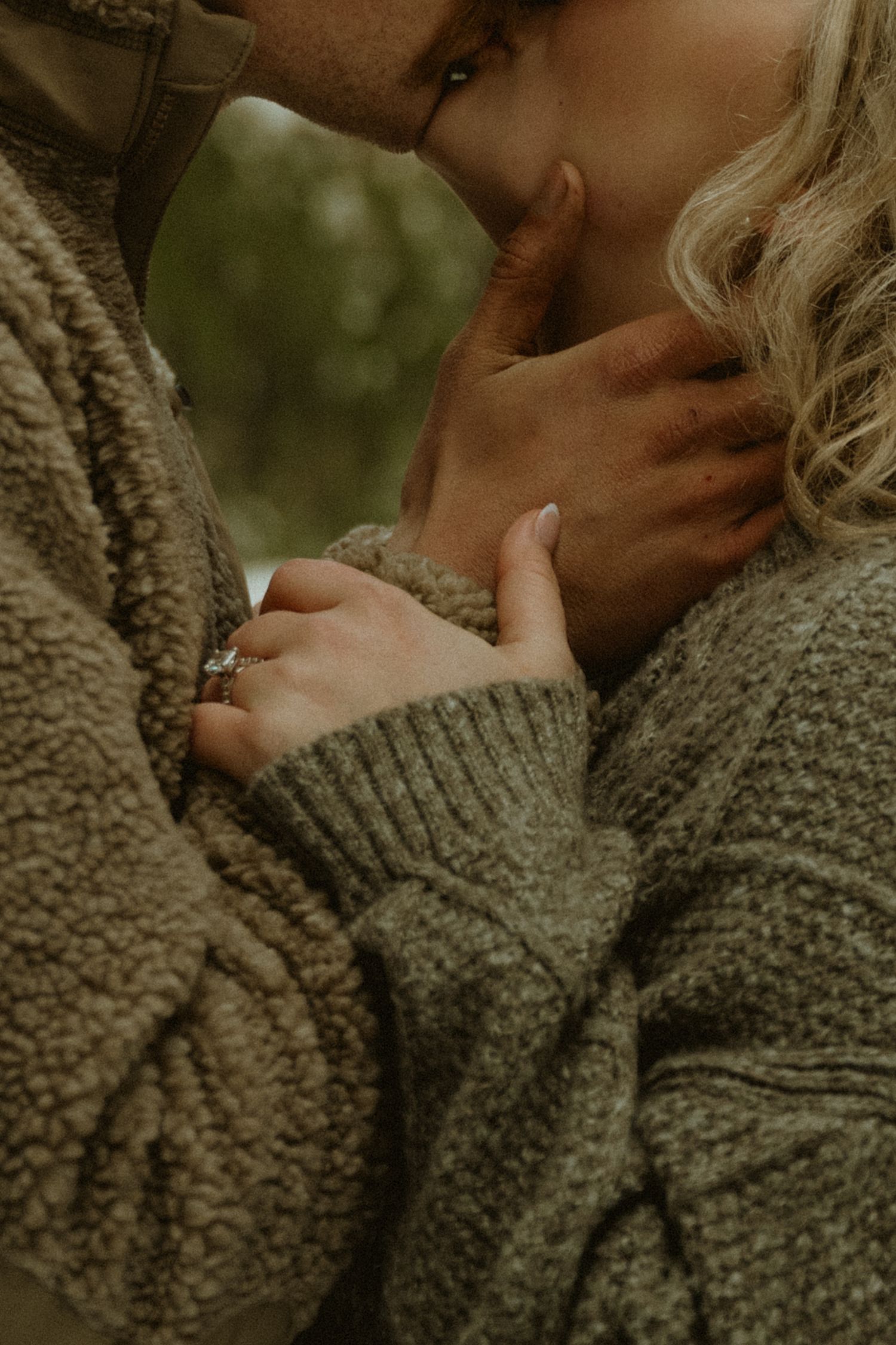 A couple in dark coats stands on a misty beach during an atmospheric photoshoot.