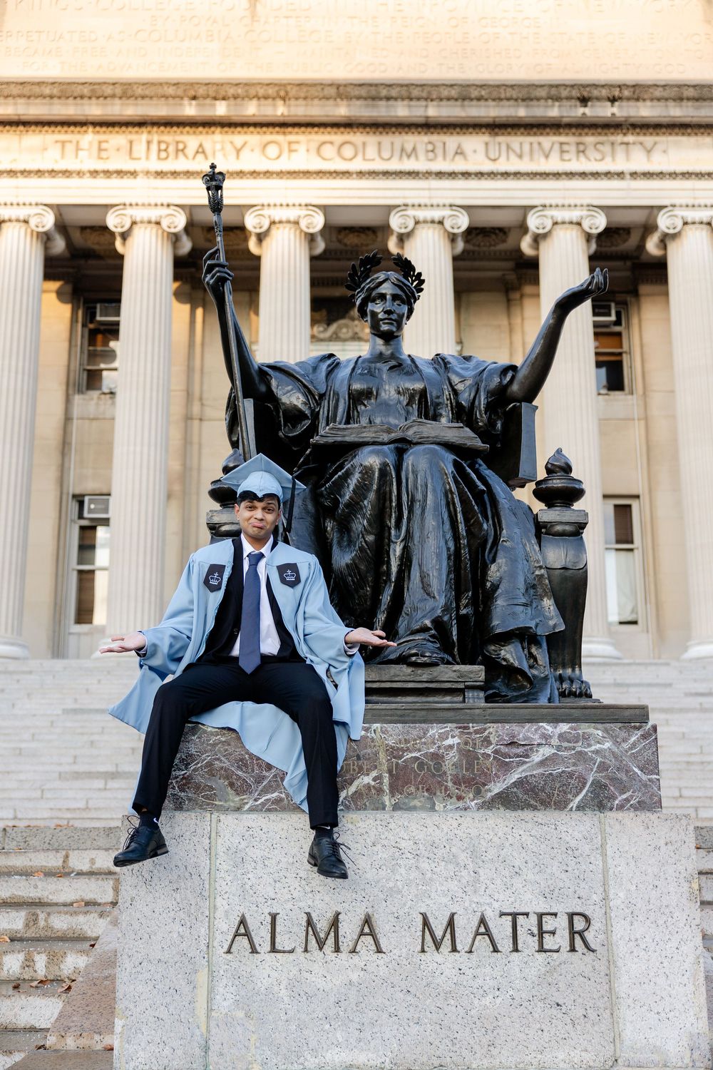 A graduate poses in front of Columbia University's iconic Alma Mater statue and library steps.