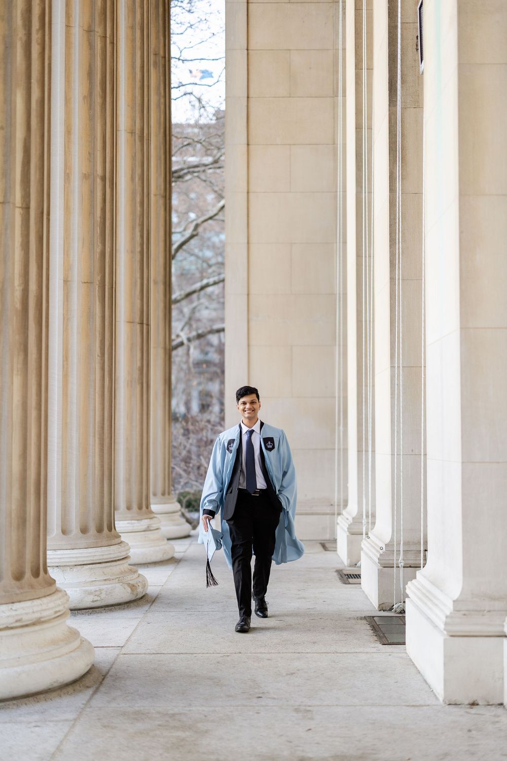A person in a suit walks between classical stone columns in an elegant architectural setting.