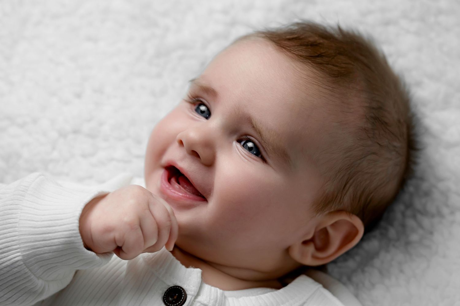 A series of four close-up shots showing a baby's joyful expressions while lying on a white blanket.