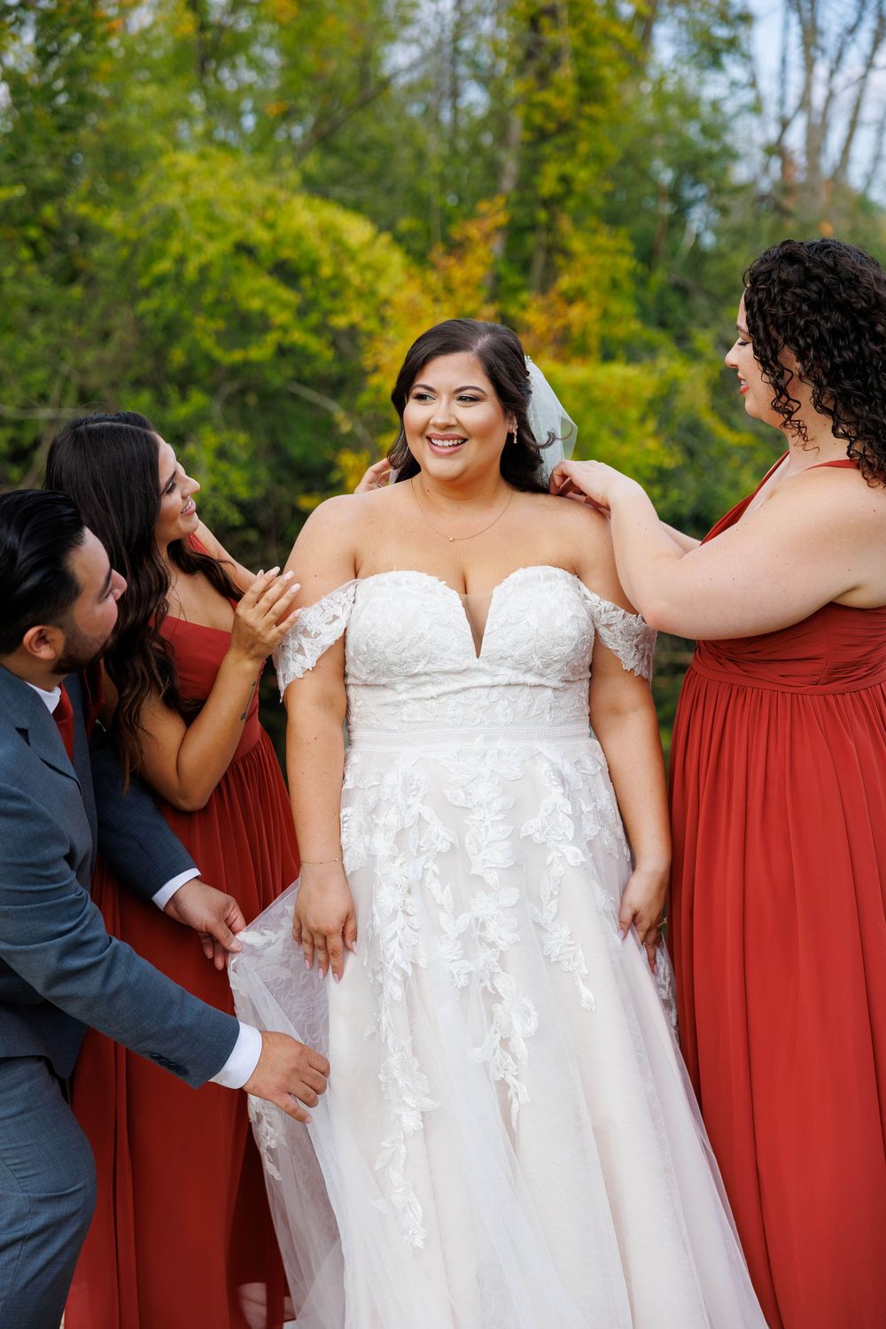 Wedding party members in burgundy dresses stand with person in white bridal gown during outdoor celebration.