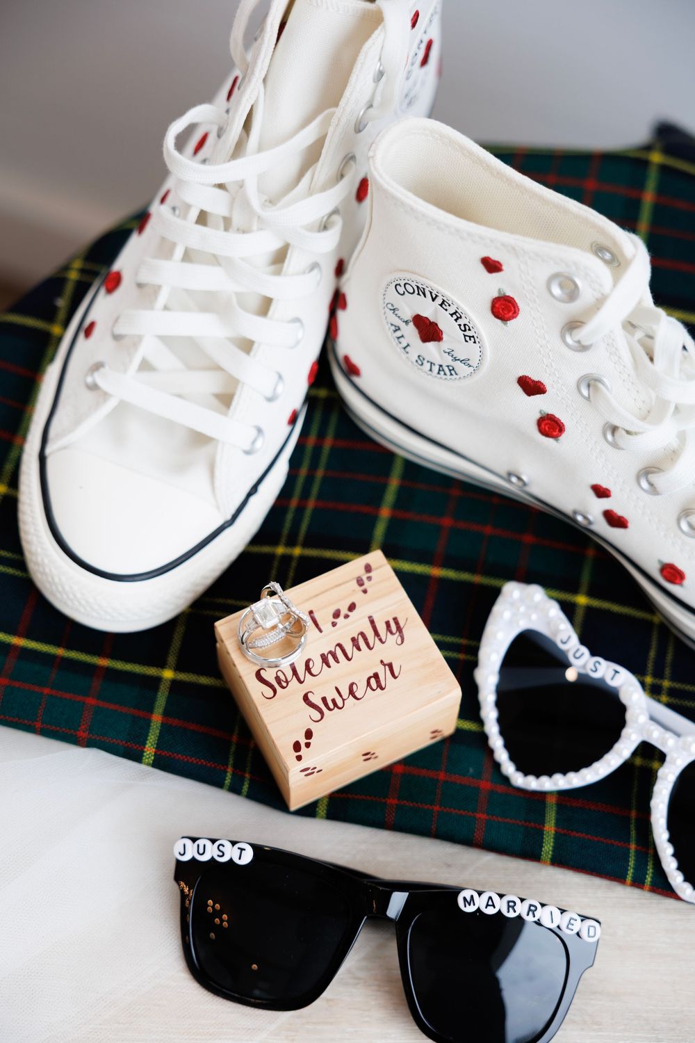 White baby Converse sneakers with heart decorations and lace trim displayed on plaid fabric.