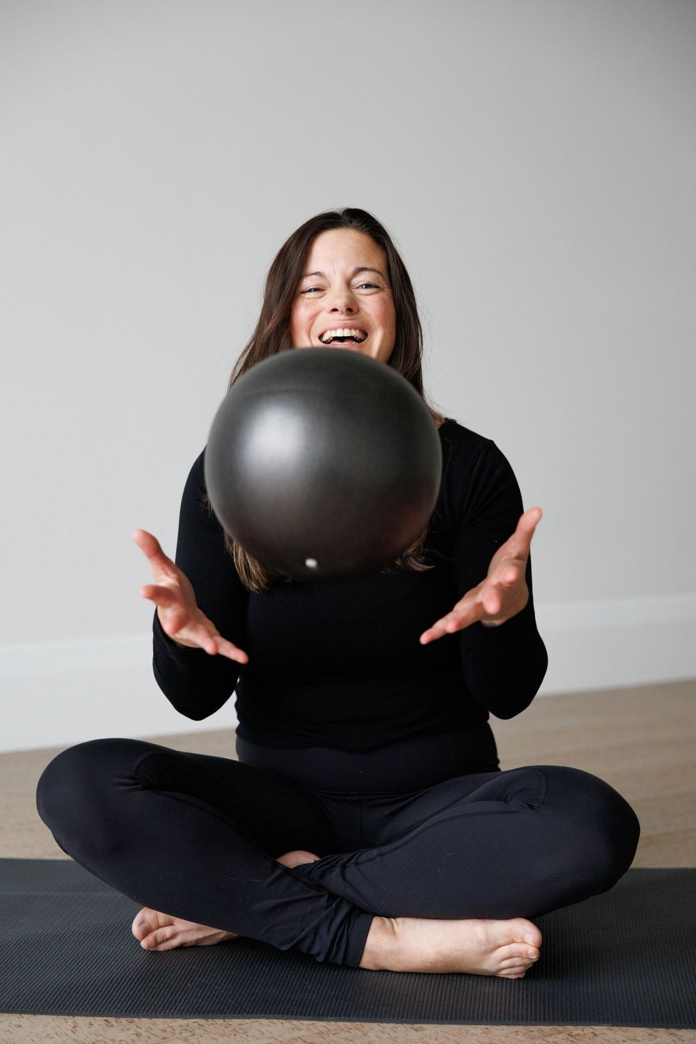 A person in black clothing sits cross-legged on a yoga mat while playfully holding a black balloon in a sequence.