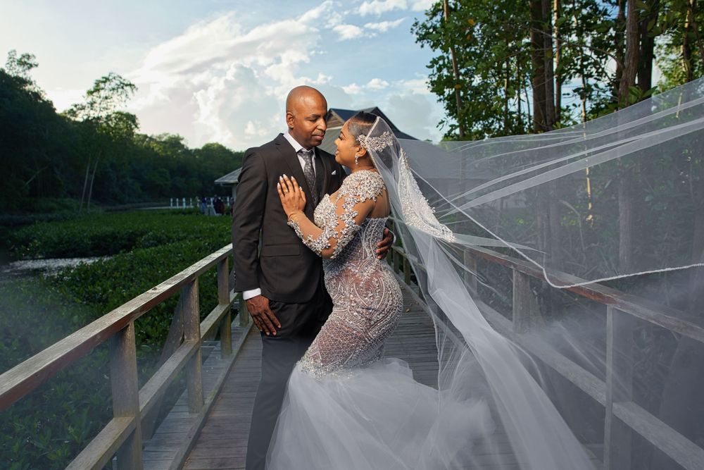 A couple in formal attire shares a romantic moment on a glass-covered bridge at dusk.