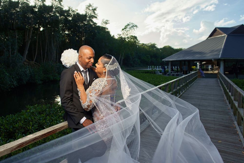 A couple shares a romantic moment with a flowing white veil on a wooden boardwalk during sunset.