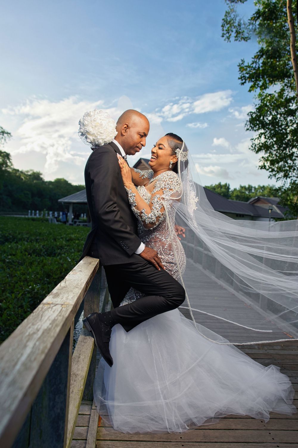 A romantic wedding couple shares an intimate moment on a wooden bridge as the bride's long veil flows in the breeze.