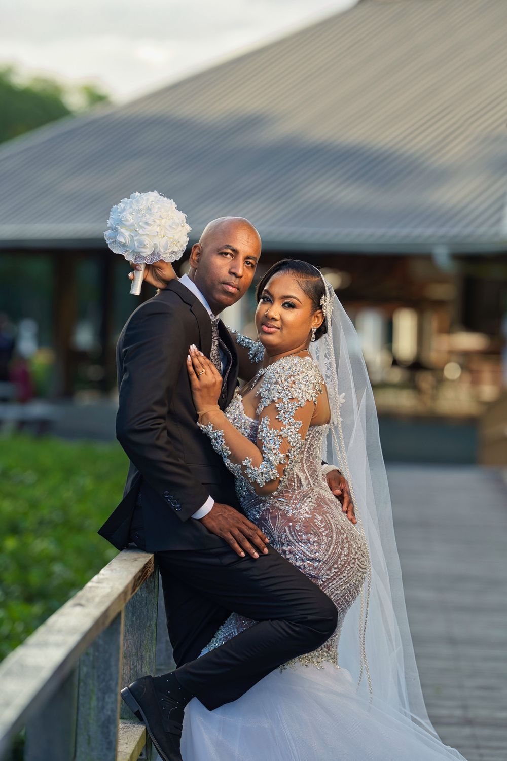Wedding couple shares intimate moments on a wooden walkway with dramatic veil movements against building backdrop.