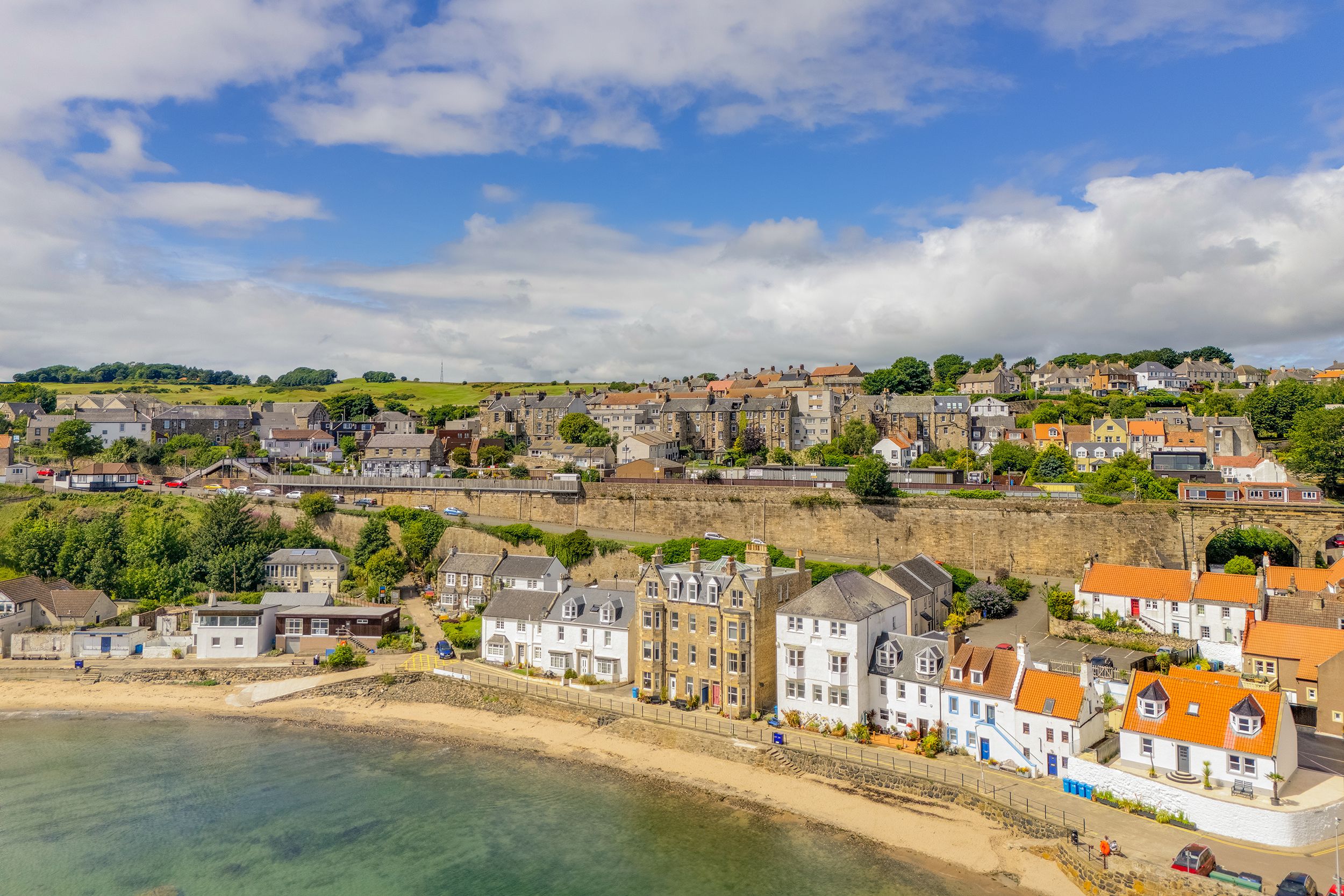 Panoramic coastal view of a seaside town with colorful buildings and sandy beach along the shoreline under blue skies.