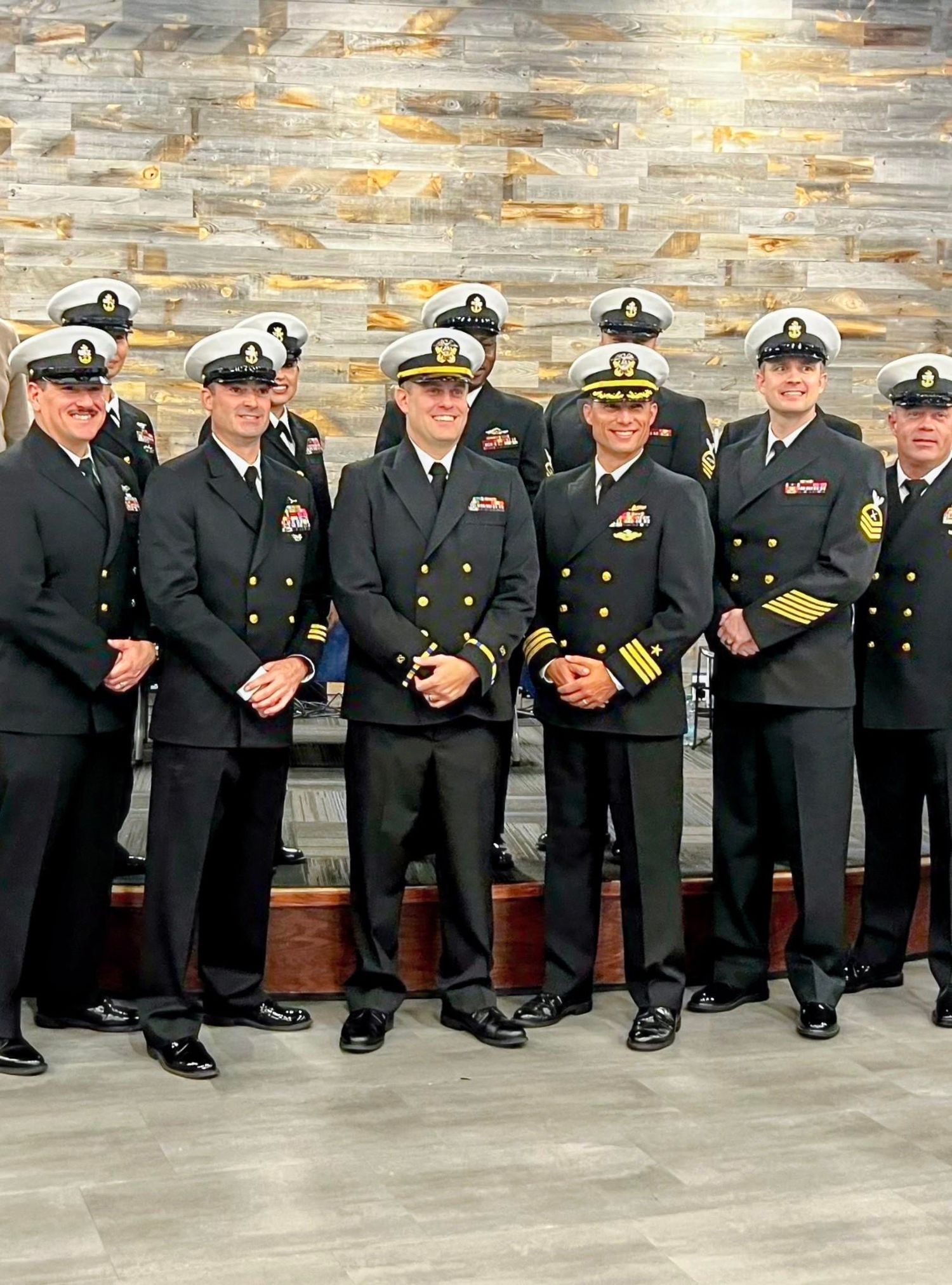 Military officers in dress uniforms sit lined up against a stone wall for a formal group photograph.
