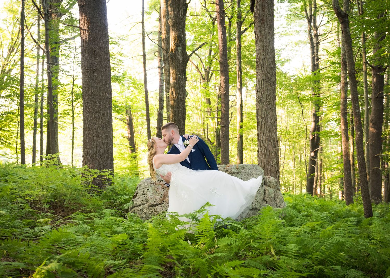 A romantic wedding couple poses together in a sunlit meadow during golden hour.