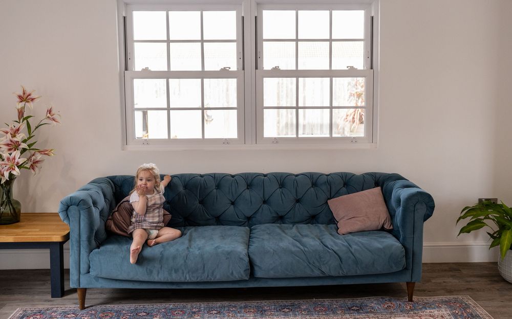 Long blue velvet couch against white wall with large windows in a bright room.