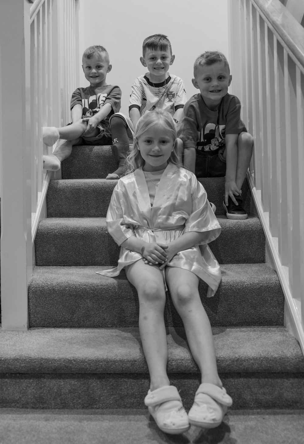Four children sitting on carpeted stairs in formal attire, captured in black and white.
