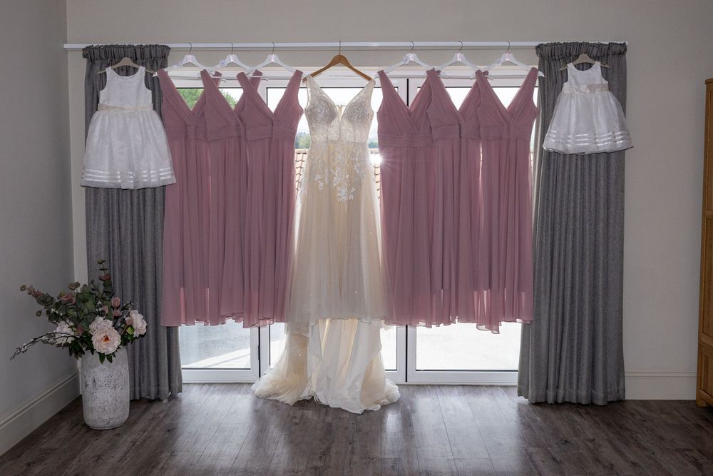 Wedding dresses and bridesmaid gowns hanging on display against white windows.