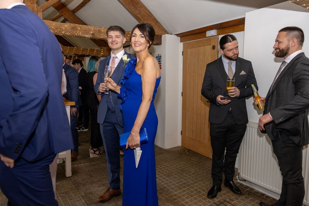 Wedding guests in formal attire socializing in a rustic venue with exposed wooden beams.