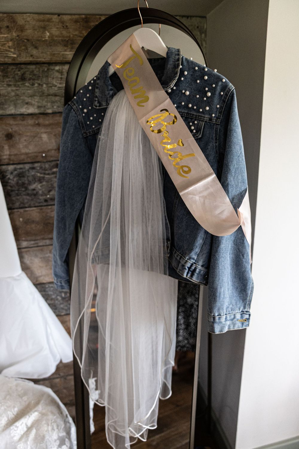 A denim jacket adorned with sparkly embellishments hangs on display with a white tulle veil and bridal accessories.
