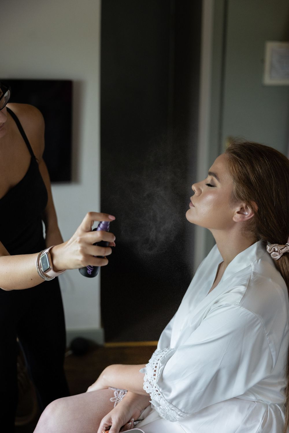 A person getting their makeup professionally applied while wearing a white robe in preparation for a special event.