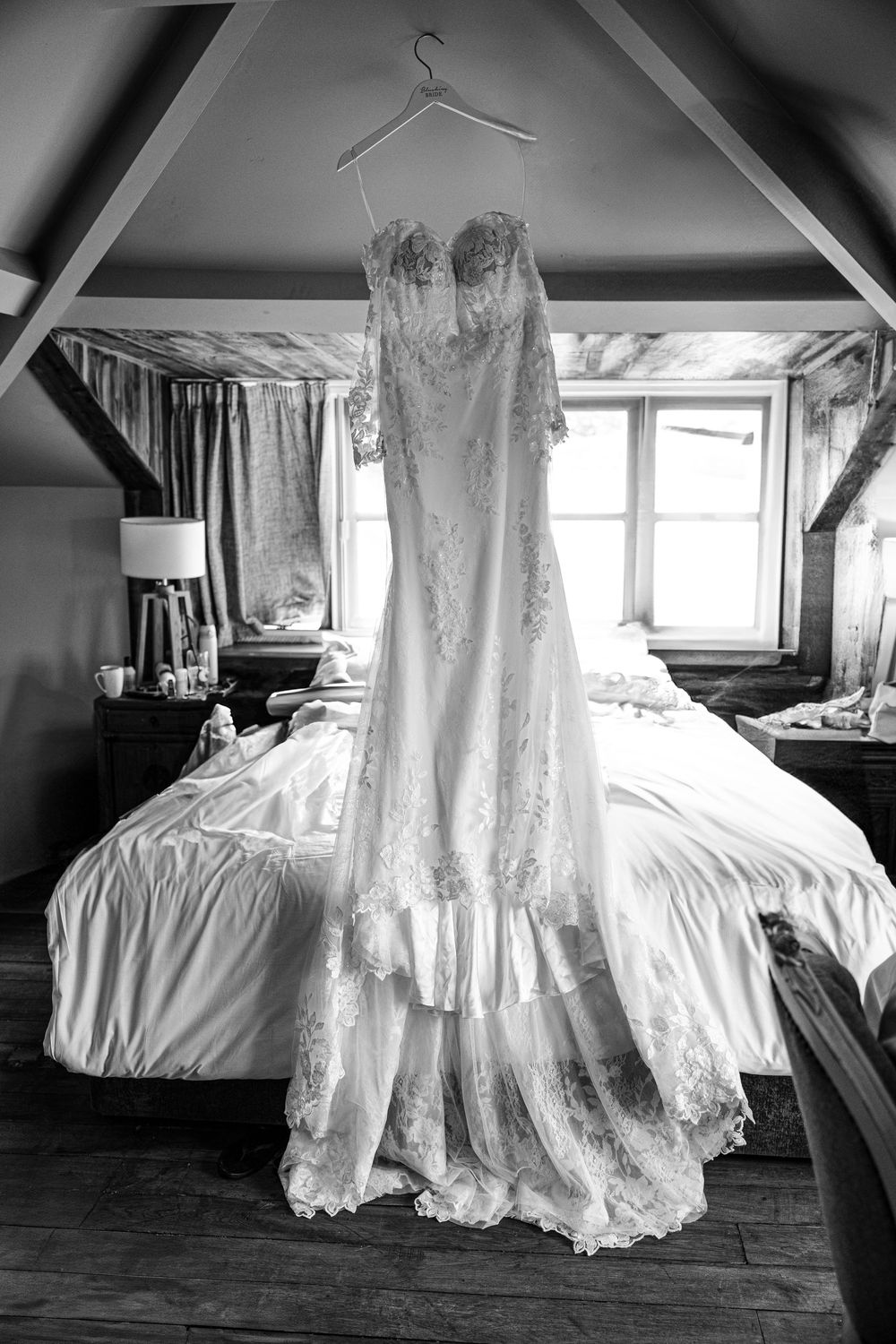 Elegant white lace wedding dress hanging in a rustic attic room with natural light.