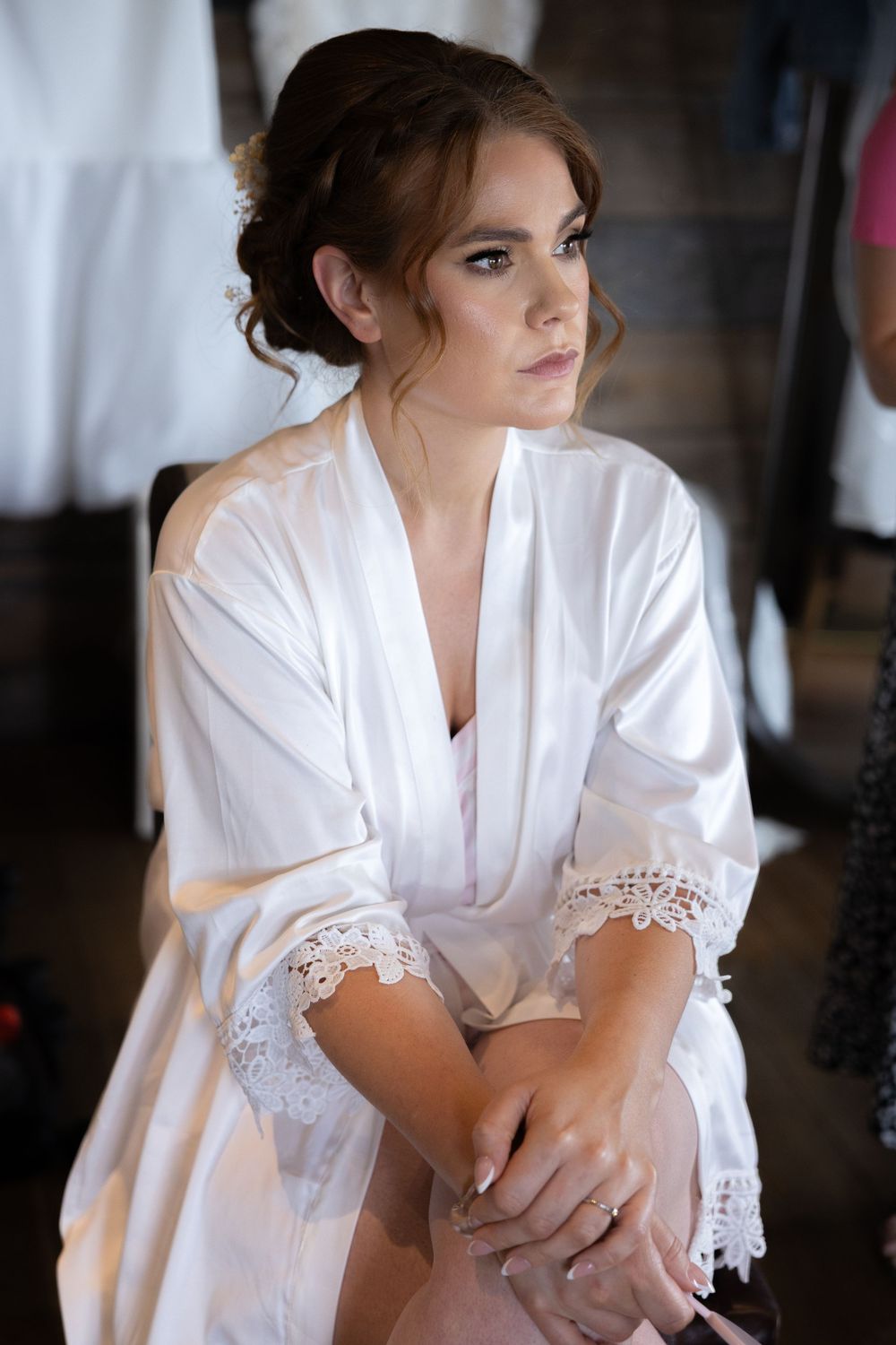 A person in a white satin robe with lace trim sits thoughtfully in preparation for a special event.
